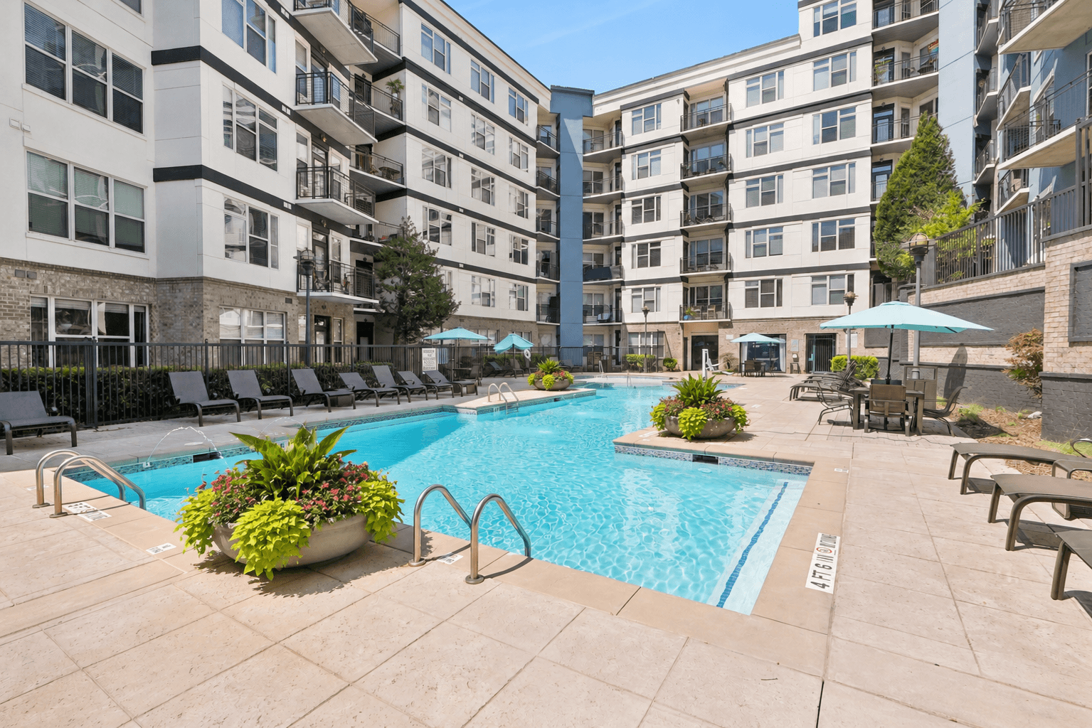 A large swimming pool surrounded by lounge chairs and umbrellas in a courtyard.